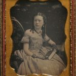 Girl in checkered dress holding a book, ca. 1855